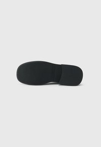 Suela de zapato de goma negra con un patrón de tracción texturizado, que presenta un talón liso y redondeado y un borde frontal plano. Diseño simple y minimalista.