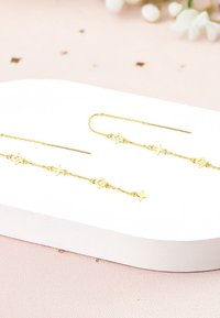 Les boucles d'oreilles pendantes en or présentent une fine chaîne ornée de formes d'étoiles et de fleurs, avec un design élégant, une finition polie et des maillons texturés.
