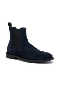 Botín Chelsea de ante azul marino con paneles laterales elásticos y suela de goma negra. Cuenta con una lengüeta para facilitar su uso. Textura suave.