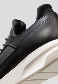 Baskets en cuir noir avec une finition lisse, dotées d'une semelle en caoutchouc blanche, d'une forme arrondie et de détails de couture subtils.