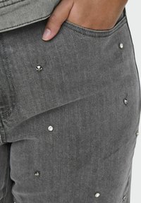 Pilki džinsai, papuošti išbarstytais rhinestone akcentais. Medžiaga pasižymi lygiu paviršiumi, klasikiniu kišenių dizainu ir laisvu siluetu.