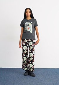 T-shirt graphique noir avec un design floral, associé à un pantalon noir ample avec des motifs floraux vibrants et des baskets noires.