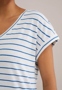 White fabric with blue horizontal stripes, short rolled sleeves, and a V-neck design. Material appears soft and slightly textured.