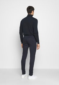 Námořnický rolák se ribovanou texturou a přiléhavým střihem, doplněný o odpovídající slim-fit kalhoty a bílé tenisky.