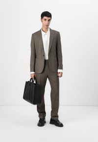 Brown plaid suit with a single-button blazer and matching trousers, paired with a white shirt and a black leather tote bag. Black shoes.