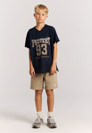 Marineblauw T-shirt met korte mouwen van mesh met "PROTEST 93" opdruk, gecombineerd met beige shorts en grijze sneakers, voorzien van witte accenten en sokken.