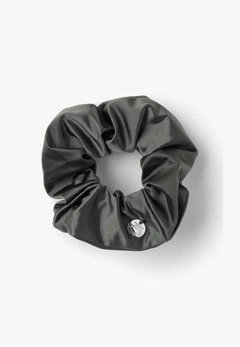 Scrunchie de satén verde con una textura suave y un diseño recogido, que presenta un pequeño acento de logo plateado en un lado.