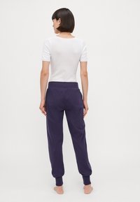 Vit kortärmad topp i kombination med lila sweatpants. Byxorna har resårmidja och cuffade fållar. Slät tygtextur.