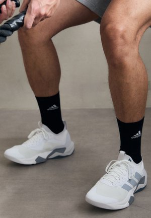 Witte sportieve schoenen met grijze accenten, een textuurmateriaal en een vetersluiting. Draagt een paar zwarte sokken met een logo.