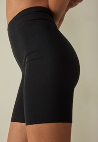 Schwarze, knielange Shorts aus einem glatten, elastischen Stoff mit einem breiten Bund. Sie verfügen über ein tailliertes Design ohne sichtbare Nähte.