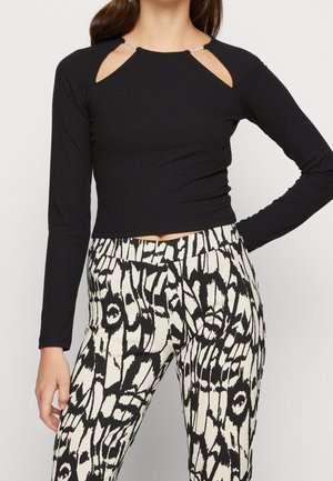 Schwarzes geripptes Langarmshirt mit einzigartigen Schulterausschnitten und silbernen Hardware-Akzenten, kombiniert mit beigen und schwarzen gemusterten High-Waist-Hosen.