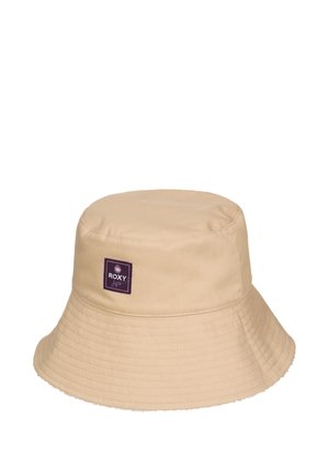 Beżowy kapelusz typu bucket z szerokim przeszywanym rondem oraz małą fioletową kwadratową naszywką z logo "Roxy" z przodu.
