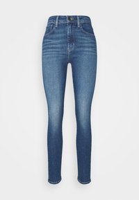 Jeans ajustados de denim azul, con una cintura alta, piernas estrechas y un acabado desgastado con sutiles arrugas en los muslos.