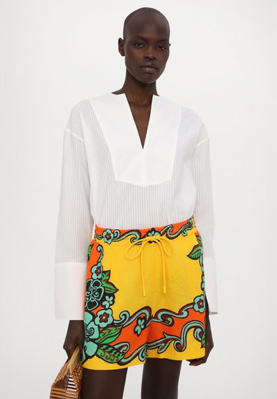 White striped shirt with a deep V-neck and wide sleeves paired with a yellow floral-patterned skirt featuring green and orange accents.