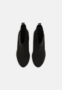 Mustat neulotut nilkkurit, joissa on teksturoidun kankaan yksityiskohtia ja pieniä kiiltäviä korostuksia. Takana vetämistä helpottava lenkki.