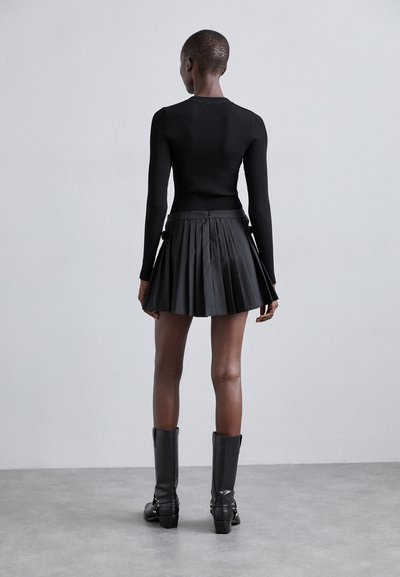 Schwarzes, geripptes Langarmoberteil kombiniert mit einem gefältelten schwarzen Minirock, getragen mit kniehohen schwarzen High Heel Stiefeln. Minimalistisches Design und Textur.