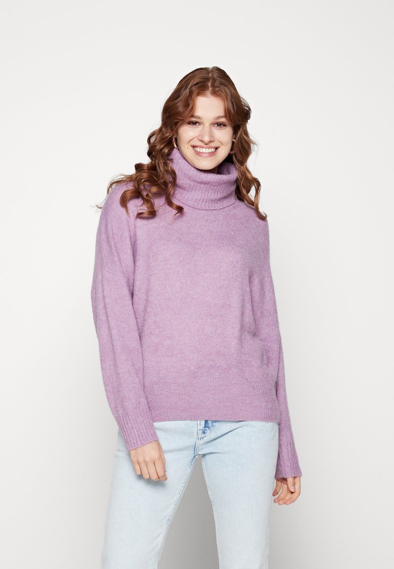 Lavendel Rollkragenpullover aus weichem, strukturiertem Material mit weiten Ärmeln und lockerer Passform, kombiniert mit hellblauen Jeans.