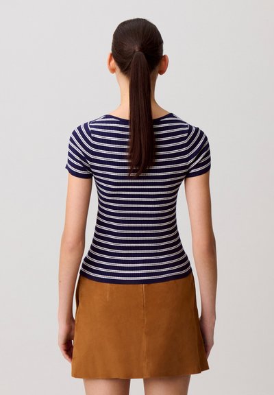 Top aderente a righe navy e bianche con maniche corte, realizzato in tessuto a costine, indossato con una minigonna in suede marrone.