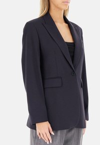 Blazer blu navy con tessuto strutturato, caratterizzato da una chiusura con un solo bottone, rever a intaglio e tasche laterali. Una vestibilità strutturata e su misura.