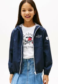 Veste légère navy avec des poignets élastiques, fermeture éclair et un intérieur à rayures blanches. Associée à un t-shirt graphique blanc et une jupe en jean.