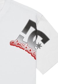Biała koszulka z krótkim rękawem z wyraźnym czarnym i czerwonym logo DC Shoes z detalem gwiazdy i kropkowym wzorem z przodu. Miękka bawełniana tkanina.
