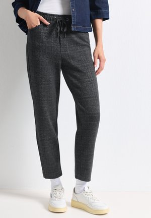 Personne portant un pantalon gris foncé à cordon, des chaussettes blanches, des baskets blanches, une chemise blanche et une veste en jean bleu foncé.