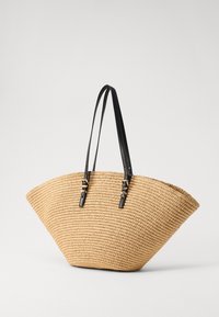 Geweven stro tote bag met een gebogen bodem, zwarte leren banden en gouden hardware accenten. Lichtgewicht en ruim ontwerp.