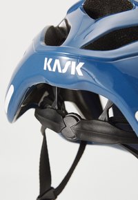 Blue Kask cycling helmet with black accents, featuring ventilation slots, adjustable straps, and a white logo on the side.