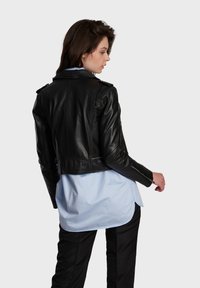 Black leather cropped jacket with shoulder epaulets and zippered cuffs, worn over a light blue blouse. Smooth texture and fitted design.