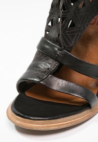 Gros plan d'une sandale en cuir noir avec des découpes à motifs, deux brides sur le pied, une semelle intérieure beige matelassée et une semelle marron clair.