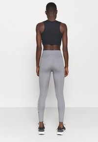 Czarny crop top bez rękawów, zestawiony z jasnoszarymi leginsami o wysokim stanie i bocznymi akcentami. Czarna para sneakersów.