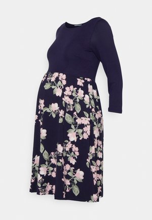 Umstandskleid mit einem marineblauen Oberteil und einem floralen Muster in Rosa und Grün. Es hat lange Ärmel und ein ausgestelltes Rockdesign.