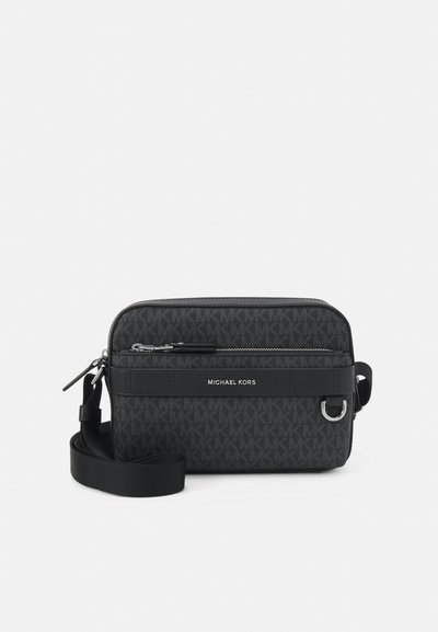 Sac cabas rectangulaire noir à bandoulière avec motif logo, poche zippée et sangle réglable. Présente une texture lisse et des garnitures en métal argenté.