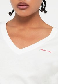 T-shirt bianco in cotone con scollo a V, caratterizzato da un piccolo logo rosso "REPLAY" sul lato sinistro del petto; texture morbida e forma aderente.