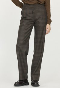 Un pantalon à carreaux bruns présente un design taille haute avec une fermeture zip, fabriqué à partir d'un matériau lisse. Détail avec des lignes orange et bleues contrastantes.