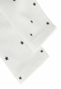 Tissu blanc avec de petits motifs d'étoiles noires. Deux manches sont présentées, présentant une texture lisse et des bords soigneusement cousus.