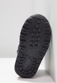 Suela de zapato de goma negra con patrones de agarre texturizados, que presenta tacos salientes e indentaciones circulares para tracción en diversas superficies.