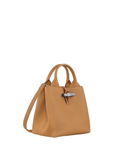 Tan leather handbag with a structured design, short handles, and an adjustable shoulder strap. Features a silver hardware clasp and textured finish.