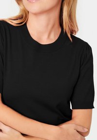 Black knit short-sleeve top with a ribbed crew neckline. Features slightly puffed sleeves and a smooth texture, creating a fitted outline.