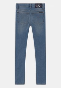 Jeans ajustados de denim azul, con dos bolsillos traseros con costuras decorativas y una etiqueta de Calvin Klein en la cinturilla.