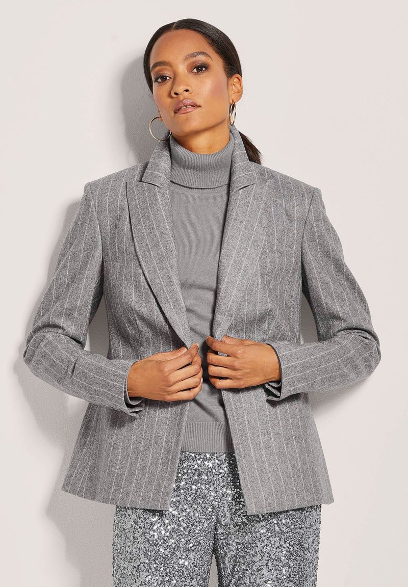 Gray pinstriped blazer with notched lapels, single-button closure, and long sleeves, paired with a light gray turtleneck and sequined pants.