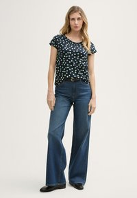 Haut à manches courtes bleu marine avec des pois verts associé à un jean large bleu et des bottes noires, présentant une taille ceinturée et une coupe décontractée.