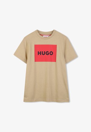Beżowy bawełniany t-shirt z krótkimi rękawami, z dużym czerwonym prostokątnym nadrukiem z napisem "HUGO" w grubych czarnych literach.