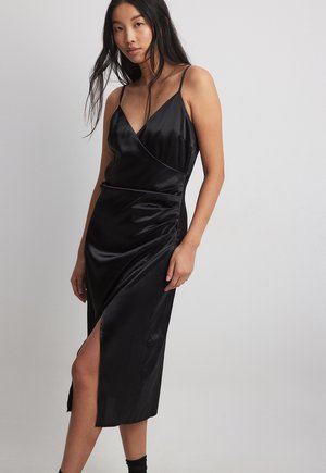 Vestido de satén negro con tirantes finos, escote en V y diseño cruzado. Presenta una abertura lateral y una silueta ajustada y elegante.