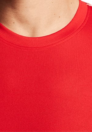 Gros plan sur le cou et le haut de la poitrine d'une personne portant un t-shirt rouge uni à col rond.