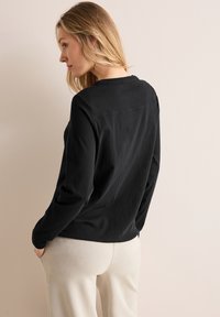 Zwarte blouse met lange mouwen van zachte stof, met een ronde hals, voorzien van een gladde textuur en een relaxte pasvorm, gecombineerd met lichtbeige trousers.