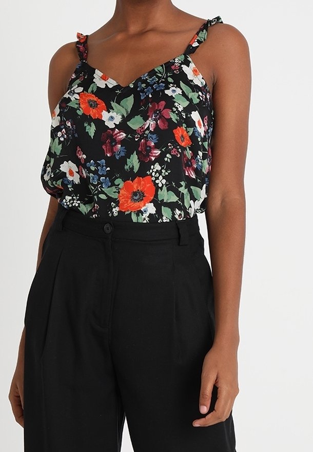 Musta kukkakuvioinen toppi, jossa on punaisia ja valkoisia kukkia, ohuet hihnat, joissa on nauha-akselit, yhdistettyinä korkeavyötäröisiin mustiin housuihin. Sileä kangas.