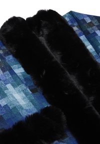 Tibetă în carouri albastre, cu nuanțe și texturi variate, accentuată cu margine din blană sintetică neagră pentru un plus de căldură și contrast.