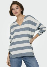 Maglione a righe in bianco e azzurro chiaro, con scollo a V e vestibilità ampia, maniche lunghe, indossato sopra jeans a vita alta.