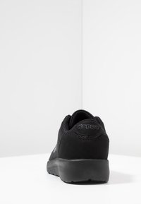 Scarpa sportiva nera con tomaia in rete, dettagli in suede e collo imbottito. Presenta una suola in gomma nera e un tallone testurizzato. Logo Kappa presente.